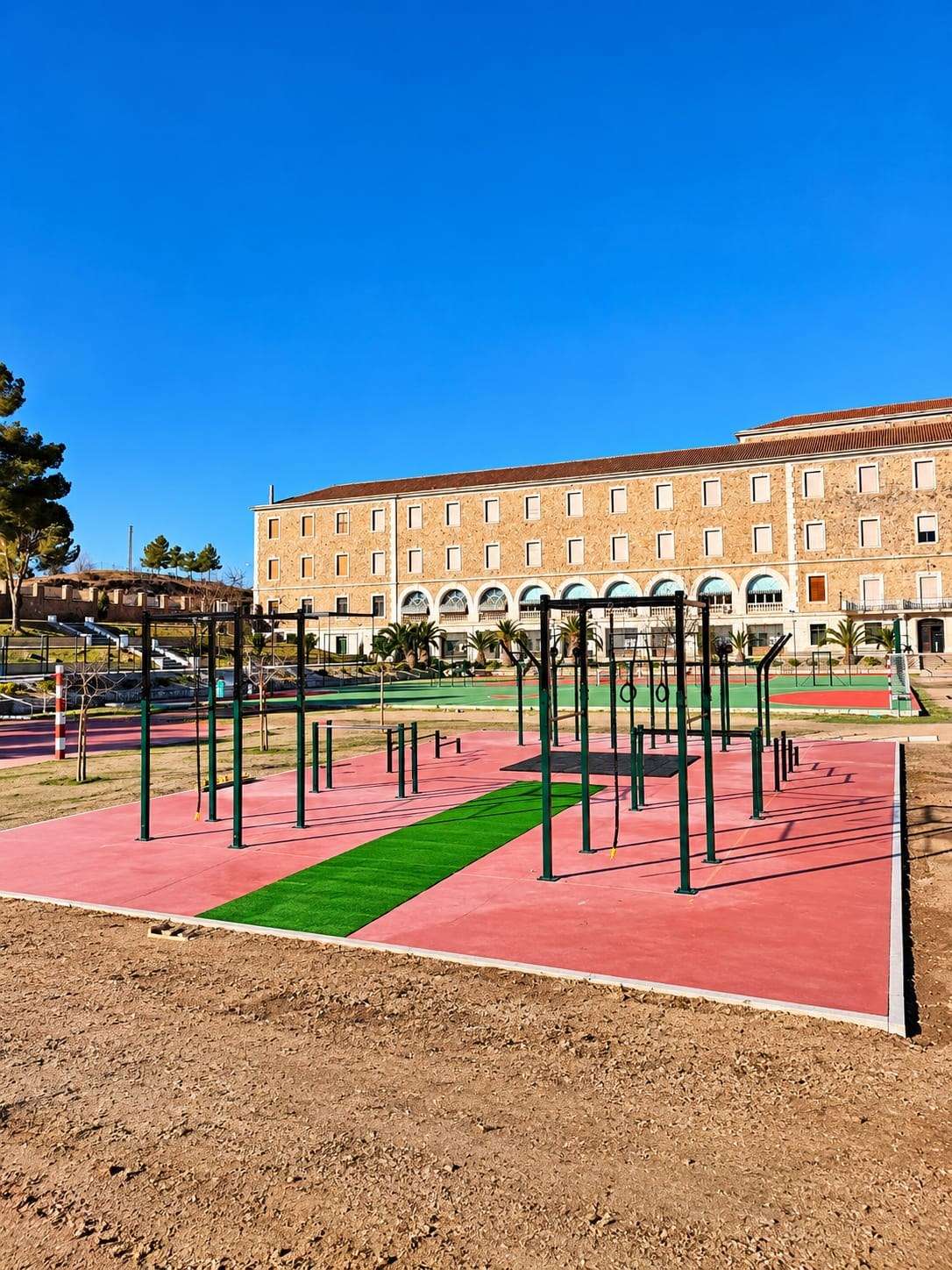 Parque de calistenia recién terminado, con suelo rojo y una franja de césped.