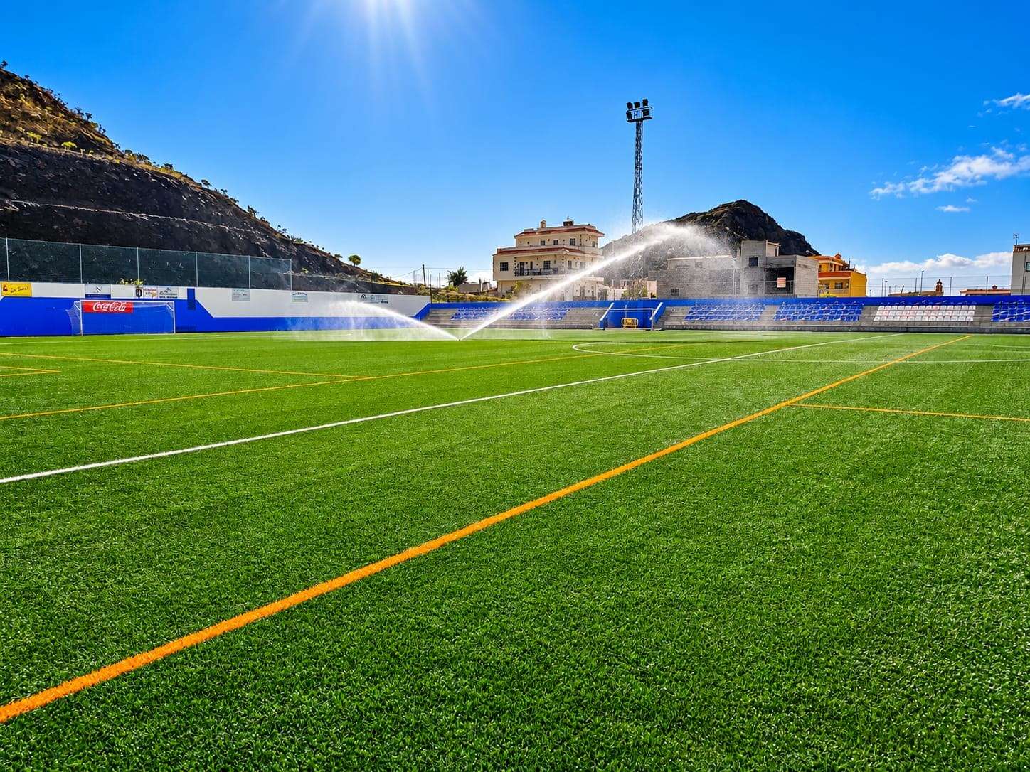Campo de fútbol de césped artificial con los aspersores en marcha.