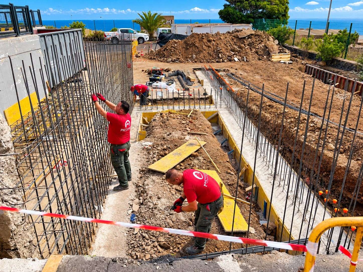 Dos operarios atan la ferralla de un muro junto a una zanja de cimentación.