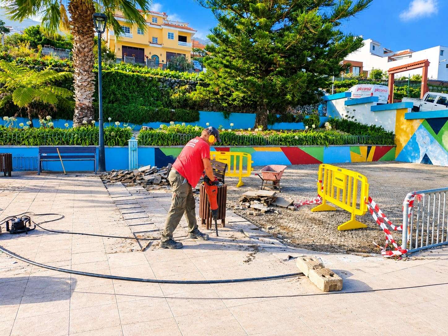 Operario levantando el pavimento de una plaza, junto a un muro pintado de colores.