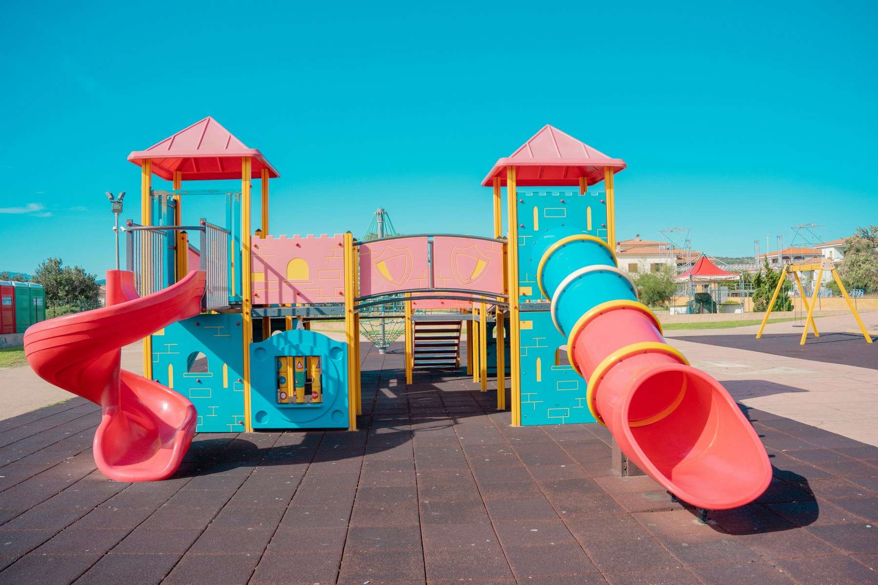 Parque infantil con torres de juego, toboganes de espiral y de tubo y suelo de caucho de seguridad.